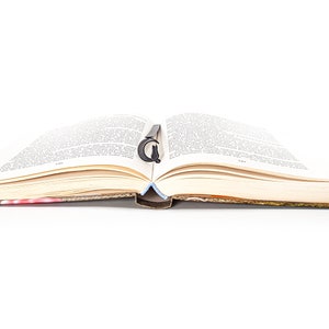 May include: An open book with a black bookmark shaped like a letter G. The book is lying flat on a white surface.
