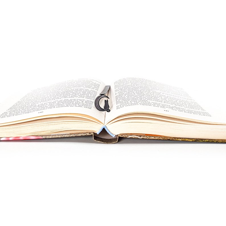 May include: An open book with a black bookmark shaped like a letter G. The book is lying flat on a white surface.