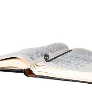 May include: An open book with a black skull bookmark. The book is open to a page with text.