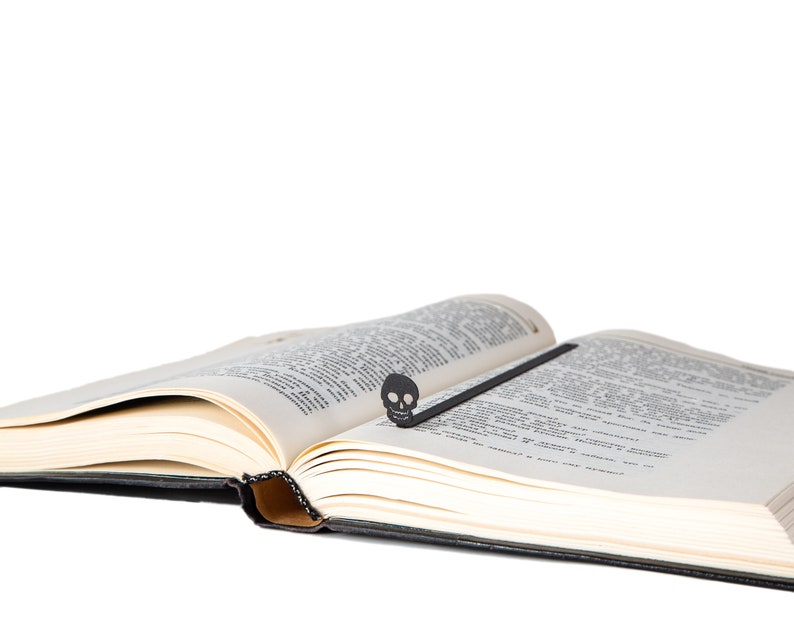 May include: An open book with a black skull bookmark. The book is open to a page with text.