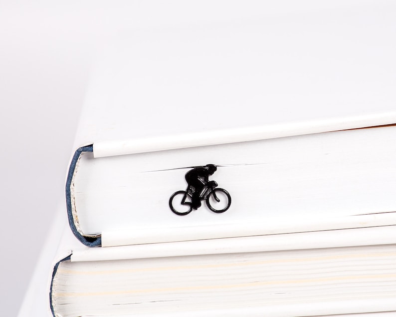 A black minimalis style metal bookmark shaped like a person riding a bicycle. The bookmark is inside a book.
