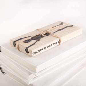 Black flat metal bookmark Skeleton on the wooden packaging block. The block says Reading is good for you.