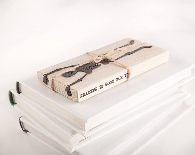 Black flat metal bookmark Skeleton on the wooden packaging block. The block says Reading is good for you.