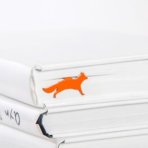 May include: A stack of white books with an orange fox bookmark on the top book.