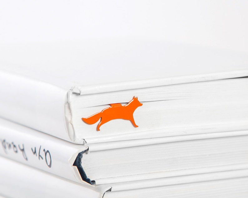 May include: A stack of white books with an orange fox bookmark on the top book.