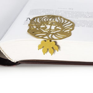 May include: Gold metal bookmark featuring a detailed cutout of a lion's face with a paw print design at the bottom.