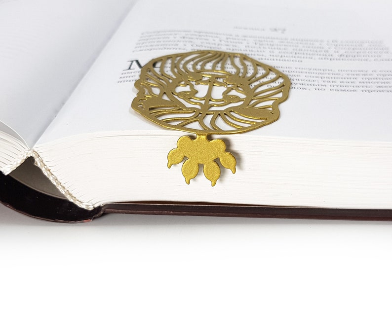May include: Gold metal bookmark featuring a detailed cutout of a lion's face with a paw print design at the bottom.