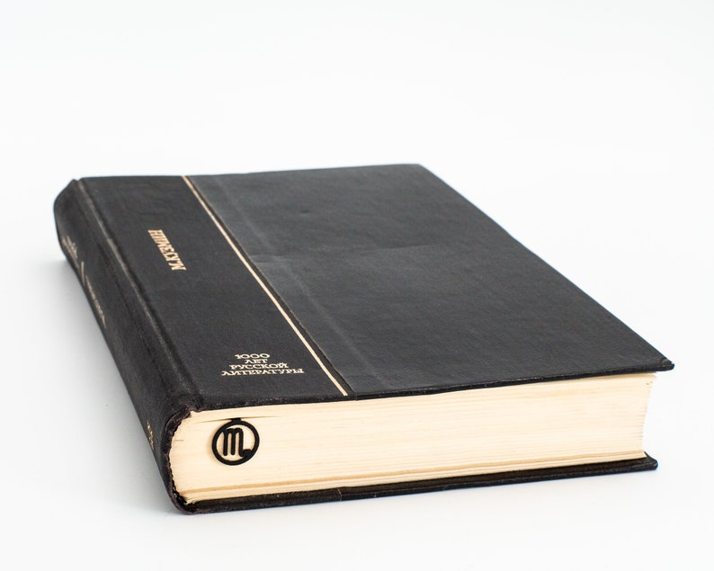May include: A black hardcover book with gold lettering on the spine that reads "LITERATURE" and "1000 лет русской литературы". A gold bookmark with the letter "M" is on the page.