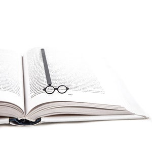 Minimalist metal page saver inspired by Bauhaus design, shaped like iconic round architect glasses, resting along the spine of an open book. A sleek tribute to modernist form and function.