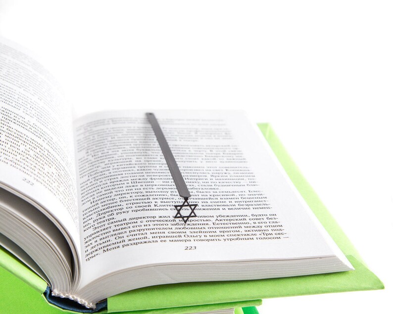 Black metal Star of David bookmark resting in an open book, placed on a green hardcover, minimalist and symbolic design.
