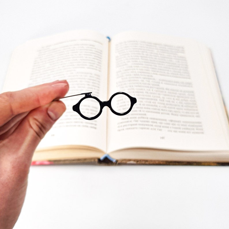 Black metal bookmark Architect's Glasses. A flat metal stick is between the pages of the book. The eyeglasses are on the side of the book. They are visible even when the book is closed.