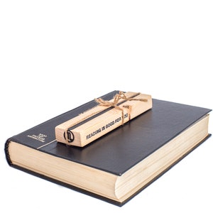 May include: A wooden bookmark with the text "Reading is good for you" tied with twine, resting on top of a closed black hardcover book.