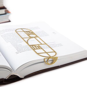 Gold metal bookmark in a geometric Bauhaus design resting on an open book — modern and elegant reading accessory with artistic flair.