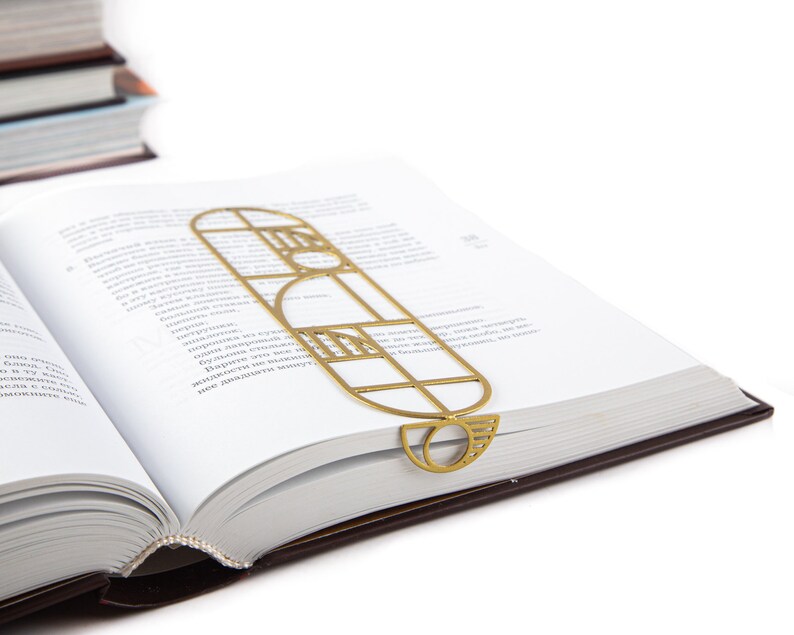 Gold metal bookmark in a geometric Bauhaus design resting on an open book — modern and elegant reading accessory with artistic flair.