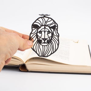 Black metal bookmark Lion head. Laser cut out of metal, the lion's head is sitting between the pages of the book. Lion paw is seen on the side of the book even when the book is closed.