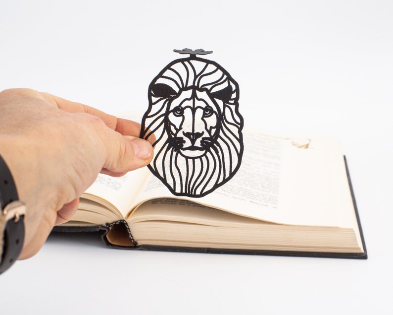 Black metal bookmark Lion head. Laser cut out of metal, the lion's head is sitting between the pages of the book. Lion paw is seen on the side of the book even when the book is closed.
