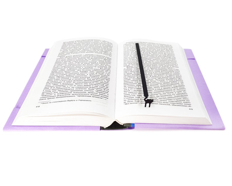 May include: An open book with text, featuring a black bookmark. The book has a light purple cover and is set against a white background. The bookmark is a simple, elegant design.