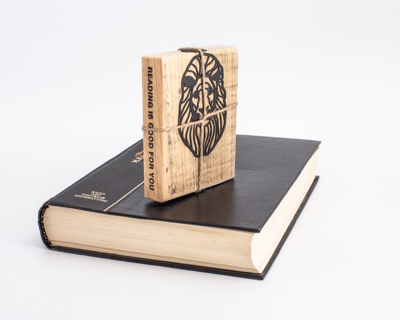 May include: A wooden book with the text "Reading is good for you" and a lion silhouette on the cover. The book is sitting on top of a black hardback book.