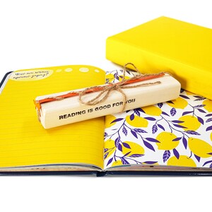 May include: A yellow journal with a lemon pattern on the cover. The journal is open to a blank page with a wooden bookmark that says "Reading is good for you".