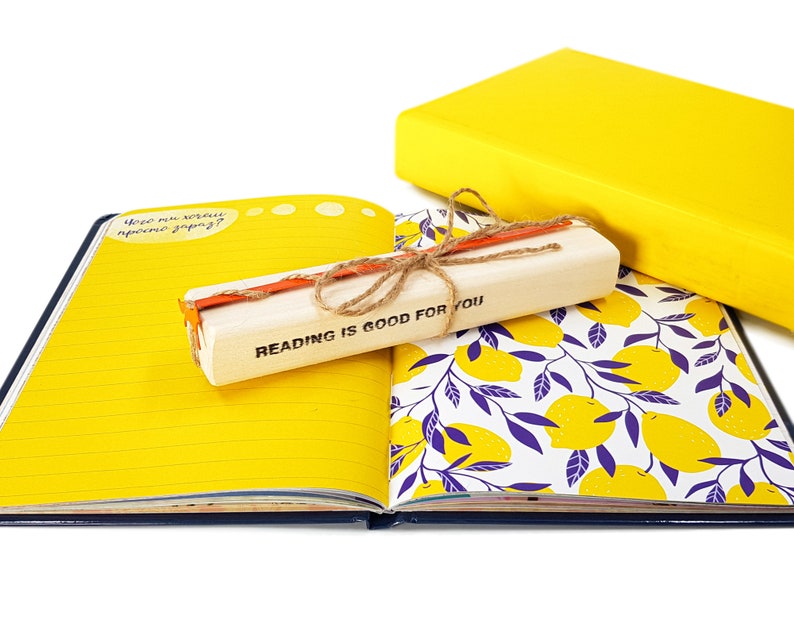 May include: A yellow journal with a lemon pattern on the cover. The journal is open to a blank page with a wooden bookmark that says "Reading is good for you".