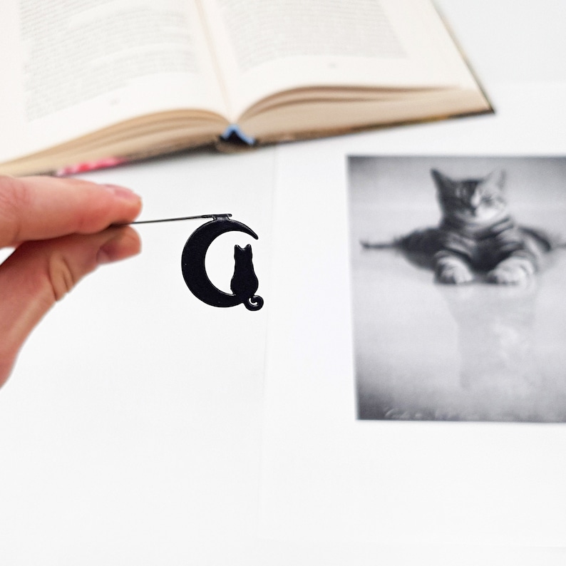 May include: Black metal bookmark featuring a crescent moon with a black cat silhouette sitting on top.