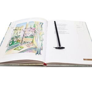 May include: An open book with a black feather bookmark. The book has a watercolor illustration of a window with a blooming tree branch and a green envelope on the left page. The right page has text and the number 35.