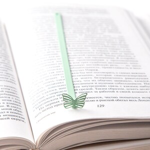 May include: A green butterfly bookmark with a light green stem is placed in a book. The book is open to page 129.