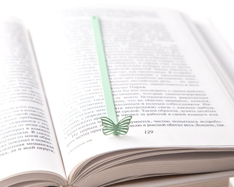May include: A green butterfly bookmark with a light green stem is placed in a book. The book is open to page 129.