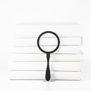 Minimalist style laser cut black metal bookmark Magnifying Glass. The magnifying glass sits between the pages of the book. Designed and made in Ukraine. Not mass manufactured.
