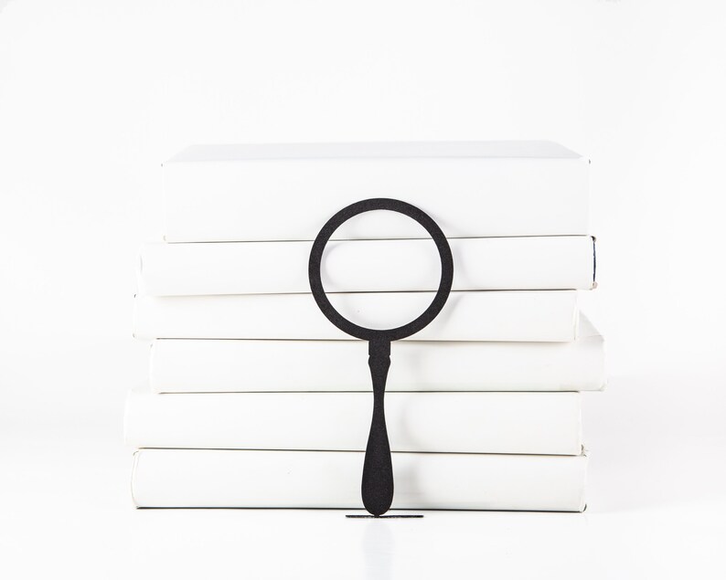 Minimalist style laser cut black metal bookmark Magnifying Glass. The magnifying glass sits between the pages of the book. Designed and made in Ukraine. Not mass manufactured.