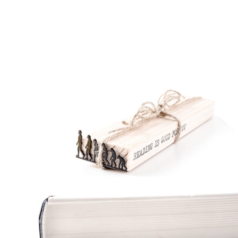 May include: A wooden bookmark with a brown twine bow and the text "Reading is good for you". The bookmark features a metal bookmark with a silhouette of the evolution of humans.