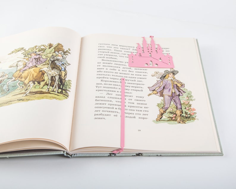 A pink castle bookmark with a pink ribbon. The bookmark is on top of an open book with illustrations of people riding horses.