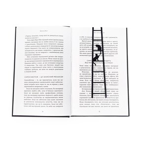 Black metal cat bookmark in the shape of a ladder placed vertically between the pages of an open book, with two cats climbing and visible above the text.