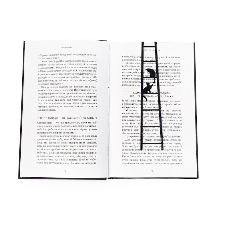 Black metal cat bookmark in the shape of a ladder placed vertically between the pages of an open book, with two cats climbing and visible above the text.