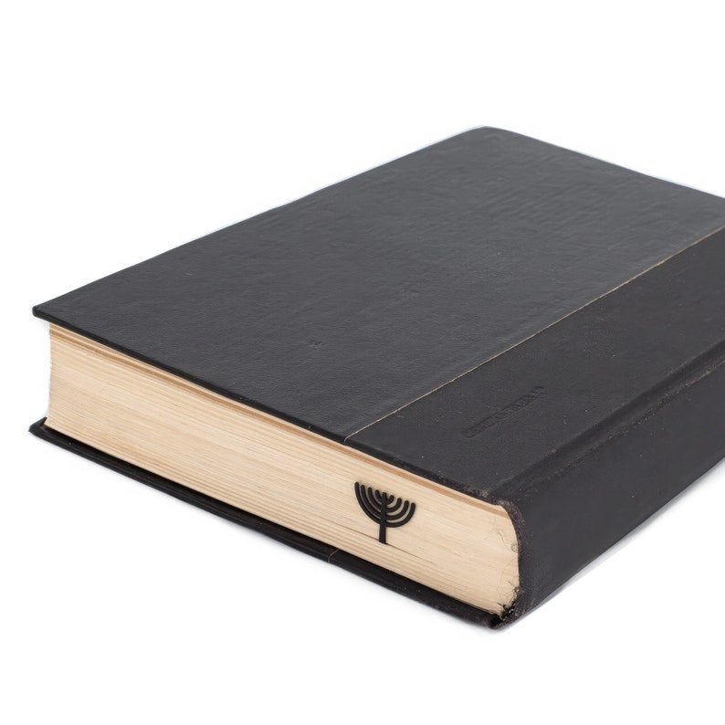 Black metal page saver shaped like a menorah, tucked into the pages of a closed hardcover book. A thoughtful Judaica gift for readers. Designed and made by Coolbookmark on Etsy.