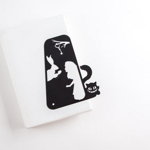 Black metal bookmark Cheshire Cat. The cat is visible on the shelf when the book divider is put in between the books - Coolbookmark.