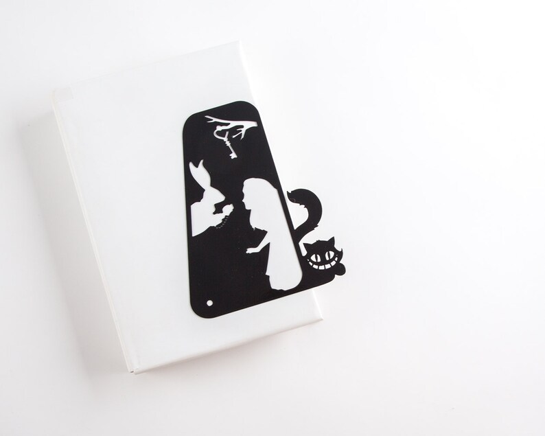 Black metal bookmark Cheshire Cat. The cat is visible on the shelf when the book divider is put in between the books - Coolbookmark.