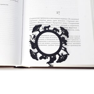 Black metal bookmark Africa. The large metal circle with African animals and trees on it. It sits between the pages of the book. The small silhouette of the African continent is on the side of the book. It is seen even when the book is closed.
