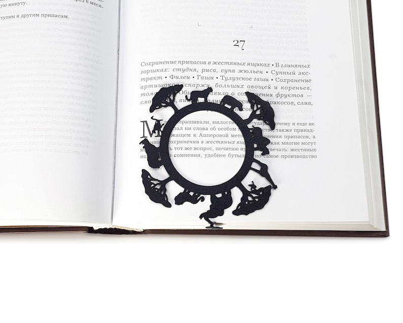 Black metal bookmark Africa. The large metal circle with African animals and trees on it. It sits between the pages of the book. The small silhouette of the African continent is on the side of the book. It is seen even when the book is closed.