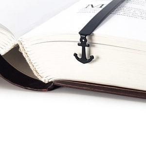May include: A black metal bookmark with an anchor design. The bookmark is placed in a book with the pages open.