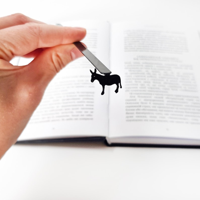 Hand holding black metal donkey bookmark above open Ukrainian text book