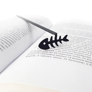 May include: A black metal bookmark shaped like a fish skeleton. The bookmark is laying on a book.
