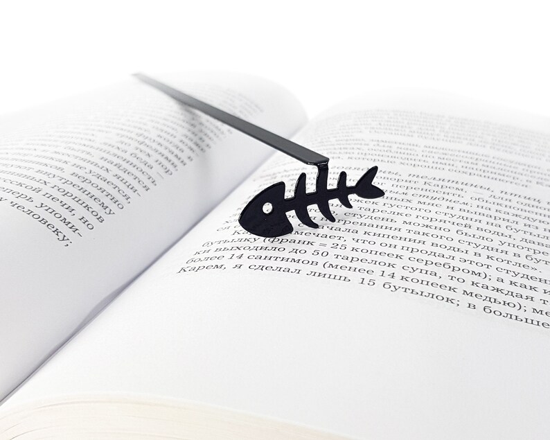 May include: A black metal bookmark shaped like a fish skeleton. The bookmark is laying on a book.