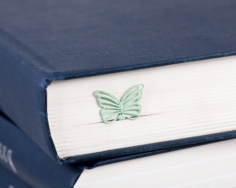 May include: A stack of navy blue hardcover books with a light green butterfly bookmark on the top book.
