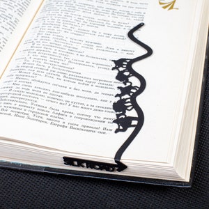 Black metal bookmark Silk Road. The loaded camels are going through hilly dessert. That part is long wavy sticklike and it stays between the pages of the book. The writing Silk Road is on the side of the book seen, even when the book is closed.