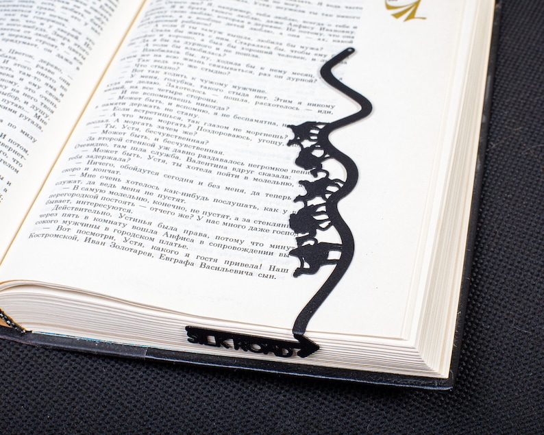Black metal bookmark Silk Road. The loaded camels are going through hilly dessert. That part is long wavy sticklike and it stays between the pages of the book. The writing Silk Road is on the side of the book seen, even when the book is closed.