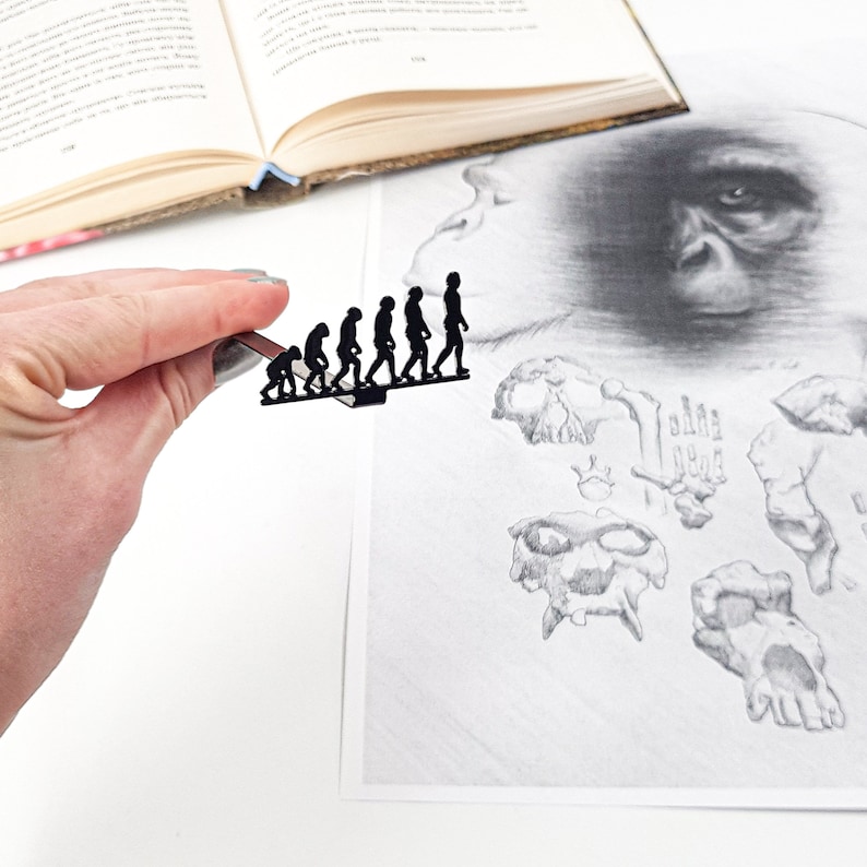 Black metal bookmark Evolution. A flat metal stick stays between the pages of the book. The silhouettes of six fingers from an ape to a human being are walking. They are visible even when the book is closed. Designed and made by us in our workshop.