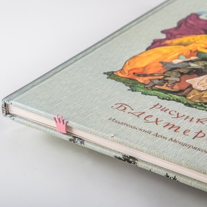 A pink crown bookmark in a book with a green cover. The book title is 'рисунки Б. Дехтерева' and the text below the title reads 'Издательский Дом Мещерякова'.