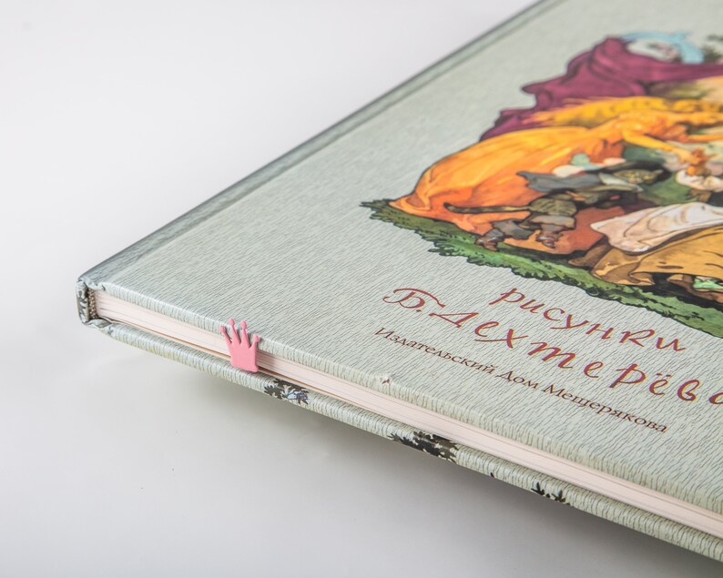 A pink crown bookmark in a book with a green cover. The book title is 'рисунки Б. Дехтерева' and the text below the title reads 'Издательский Дом Мещерякова'.