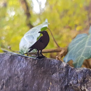 Black metal raven-shaped page saver perched on a rock with ivy leaves in the background. A mystical, forest-inspired gift for readers drawn to folklore and dark nature aesthetics.